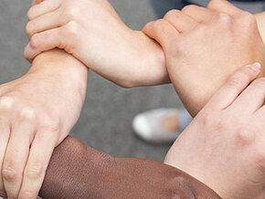 Kreis aus vier Händen wird gebildet indem Personen einander an Handgelenken umfassen
