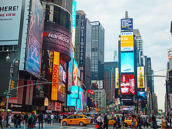 Der Times Square in New York mit vielen Menschen, Autos, Hochhäusern, Werbetafeln und bunten Leuchtreklamen