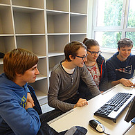 Vier Schüler und Schülerinnen vor ihrem gemeinsamen Computer.