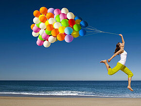 Maedchen mit bunten Luftballons springen am Strand c iko Clipdealer Mädchen mit bunten Luftballons vor blauem Himmel