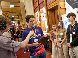 Jugendliche in der Parlamentsbibliothek bei einem Workshop. Eine Bursche mit Klemmbrett stellt fragen, eine Bursche mit Mikro und Kopfhörer zeichnet nimmt die Frage auf.