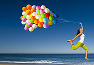 Ein Mädchen springt mit vielen bunten Luftballons einen Strand entlang.