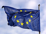 Die Flagge der Europäischen Union weht an einem Fahnenmast im Wind vor einem leicht bewölkten Himmel.