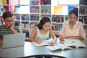 Jugendliche lernen in einer Bibliothek, vor ihnen Bücher und ein Laptop