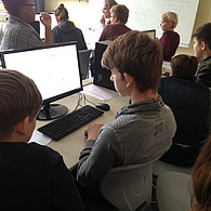 Schüler und Schülerinnen vor ihrem gemeinsamen Computer mit Blick auf den Bildschirm.