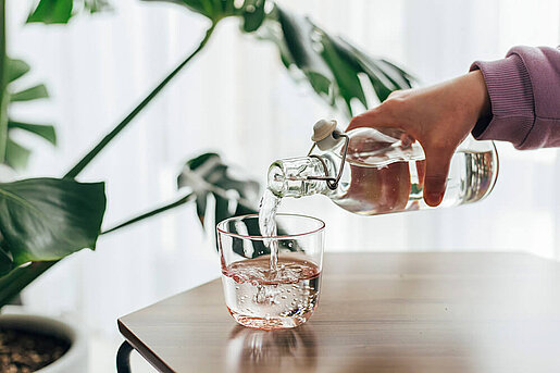 Eine Hand füllt ein Glas Wasser aus einem gläsernem Krug