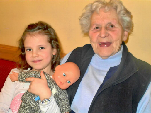 Frau Riediger mit ihrem Urenkel Lina als junges Mädchen, Lina hält eine Puppe.